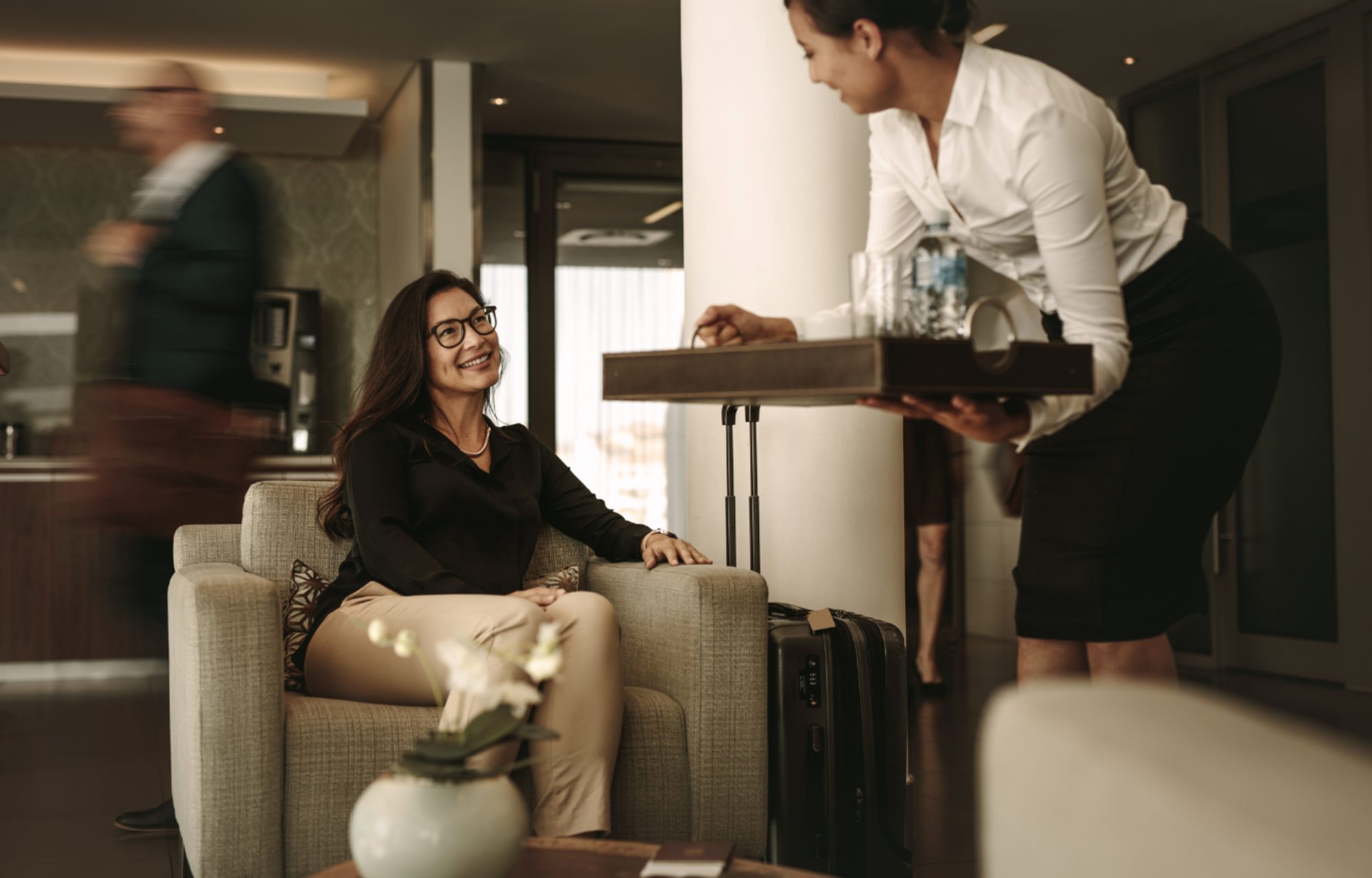 A traveler with luggage being served in a reciprocal club's lounge